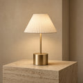 Aetheris Atelier Cordless Brushed-Brass and Pleated Alabaster Architectural Table Lamp casting warm 2700K pool of light on travertine surface