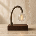 Aetheris Atelier Magnetic Levitating Walnut and Warm-Filament Architectural Desk Lamp suspended in mid-air above solid walnut pedestal on travertine stone